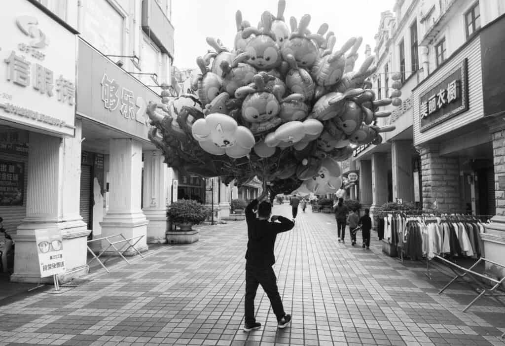 Man with balloons in small city in guangdong China. Black and white empty street