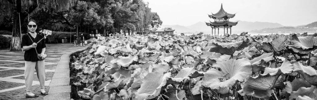 Selfie at Hangzhou west lake, Lady with phone, and selfie stick, lake side, china, Lillie’s, pagoda, trees, black and white