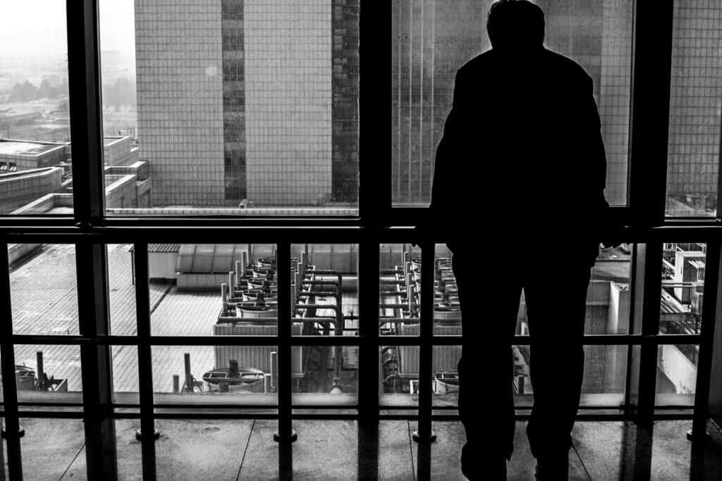 Old man stands next to window, looking out at the hospital, daytime, china