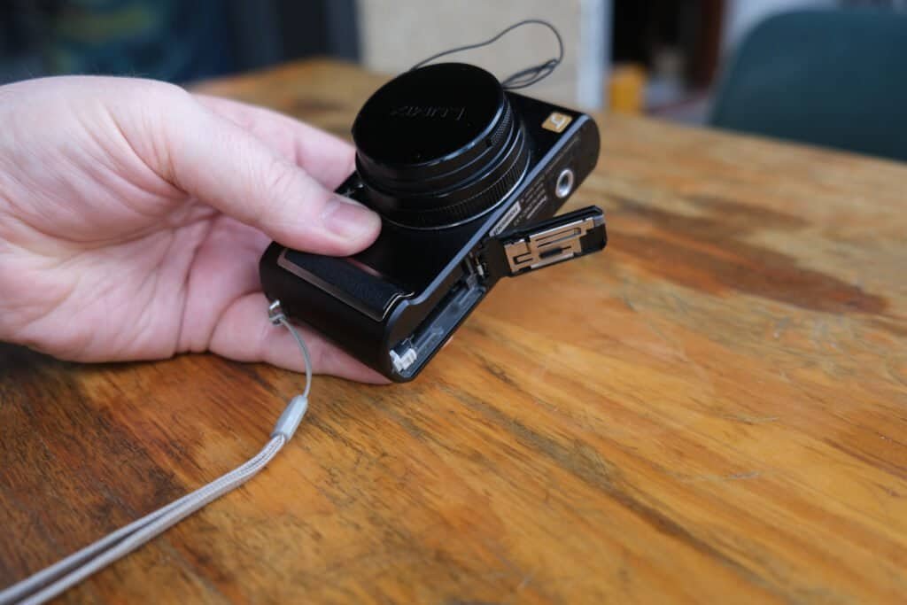 Panasonic LUMiX DMC LX3 in leather case hand table lens cap strap bottom view Battery door open