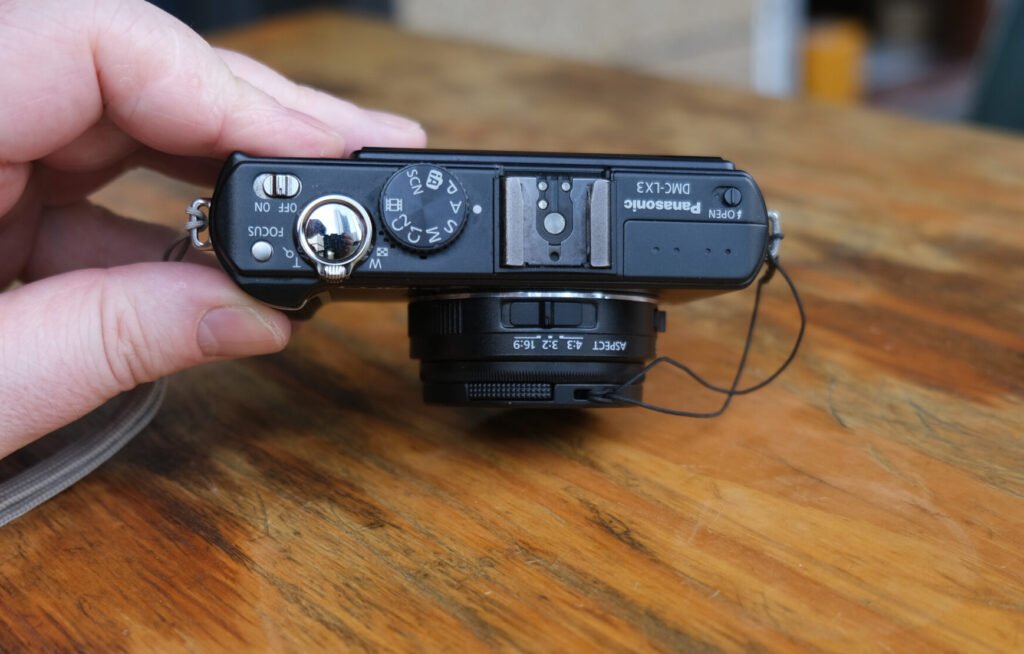 Panasonic LUMiX DMC LX3 in leather case hand table lens cap strap bottom view Battery door open