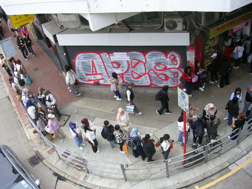 Hong Kong Mong Kok people women men gather and walk on a busy street in Mong Kok Hong Kong daylight Sunday graffiti in the back ground